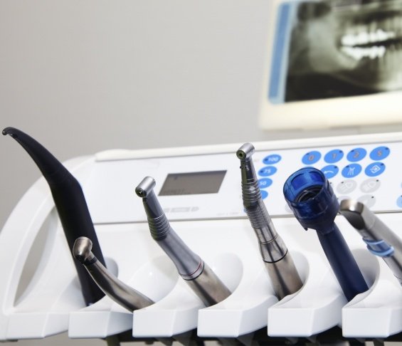 Row of dental instruments with X ray of teeth on computer screen in background