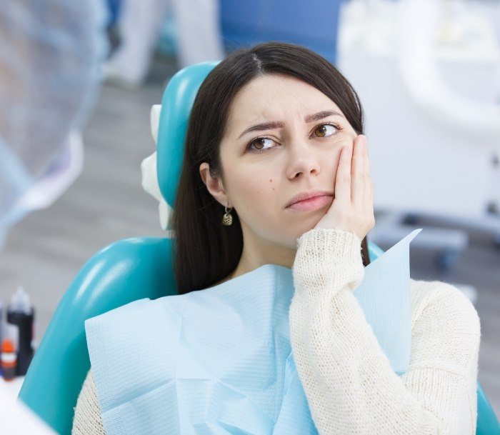 Woman in dental chair holding her cheek in pain