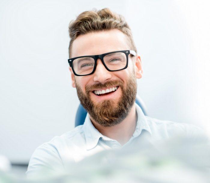 Bearded man in dental chair smiling after endodontic retreatment in Jersey City