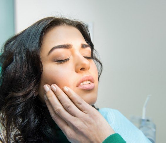 Woman in dental chair touching her cheek in pain