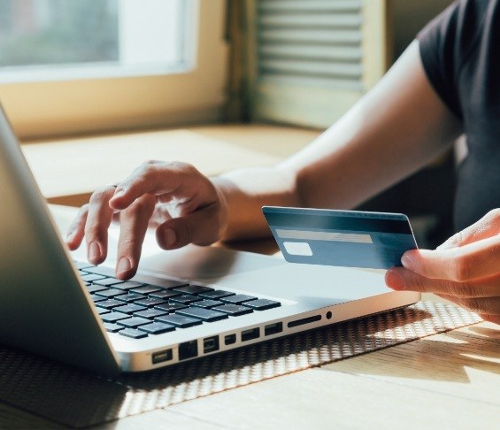 Person typing on laptop while holding a credit card in one hand